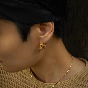 Model wearing gold woven multi-hoop earrings and a flat snake bone chain necklace