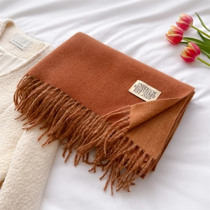 Detailed shot of folded orange cashmere scarf with fringe and brand label on white fabric
