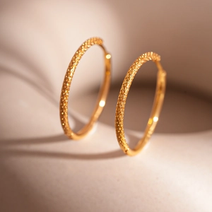 Minimalist gold geometric hoop earrings with textured hammered finish on beige pedestal