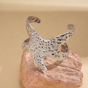 Close-up of a silver starfish cuff bracelet with textured grain on a rustic rock