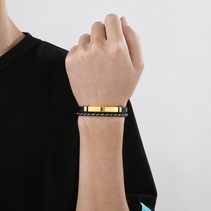 Close-up of men's black braided leather bracelet with a polished gold metal plate bar