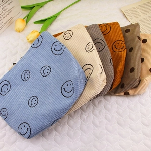 Corduroy makeup bags with smiley faces and dots in various colors on white table