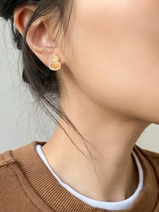 Close-up of gold gourd stud earrings with zircon stones worn by a model in soft lighting