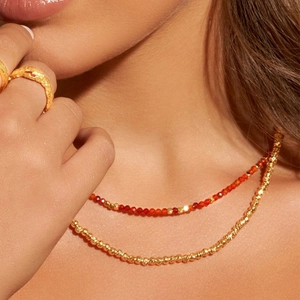 Close-up of layered red crystal beads and golden textured necklaces on model neck