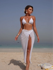 Three-piece white bikini set with halter top and mesh beach skirt for summer vacations