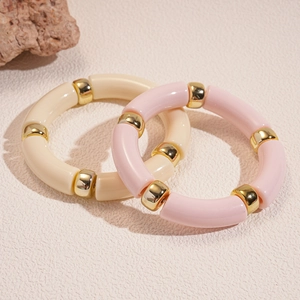 Dettaglio di braccialetti in acrilico crema e rosa chiaro con perline in metallo dorato