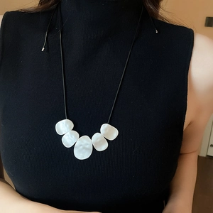 Irregular white shell-like geometric pendants on a black leather cord worn by a model