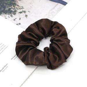 Close-up of a large dark brown satin scrunchie with smooth silk texture on a magazine