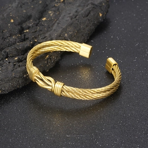 Detailed view of golden twisted cable wire bracelet with knot charm on a dark rock surface