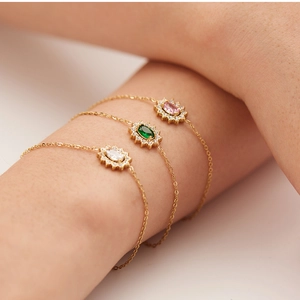 Close-up of stacked gold bracelets featuring pink, green, and white zircon crystals