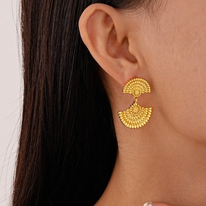 Close-up of a model wearing gold fan-shaped textured earrings with a metallic finish