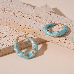 Detail of light blue marble resin hoop earring with a tiny rhinestone on travertine