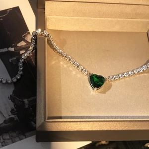 Detail shot of heart-shaped emerald green pendant on a silver-tone tennis chain in box