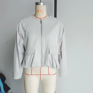 Detail of light grey bomber jacket with metal zipper closure and utility flap pockets