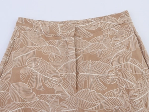 Detail of tan cotton-linen shorts with white leaf print, showing waistband and pocket
