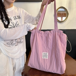 Detail of pink pleated tote bag featuring a white logo label and soft shoulder straps