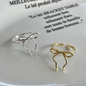 Detailed macro view of bow-knot ribbon rings in silver and gold on a ceramic tray