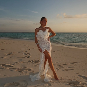 Robe longue en dentelle blanche à volants avec fente haute sur plage au coucher du soleil