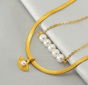 Detail of layered gold snake chain and pearl necklace with a ginkgo leaf pendant