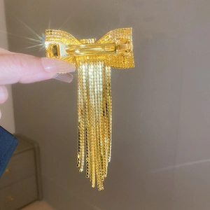 Détail d'une pince à cheveux dorée ornée de strass et de longues franges fluides