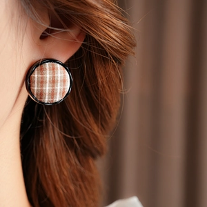 Close-up of a model wearing a round red-brown checkered fabric stud earring with black trim