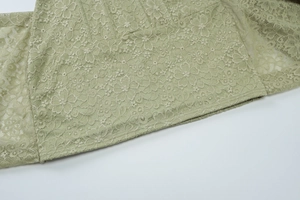 Dettaglio macro della trama in pizzo floreale e del tessuto verde chiaro del vestito