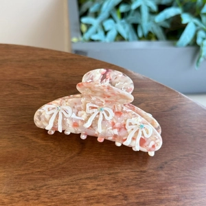 Close-up of pink marble acetate hair claw clip with white 3D bows and colorful rhinestones
