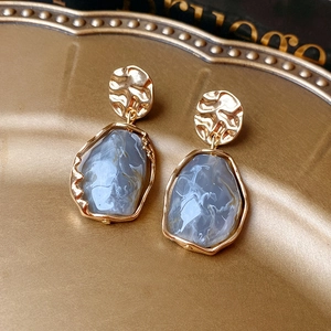 Détail de boucles d'oreilles dorées avec résine marbrée bleu-gris sur un plateau en métal