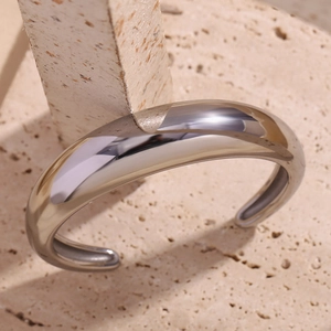 Close-up of a minimalist silver open bangle on a textured stone and geometric pedestal