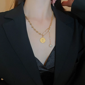Detail of vintage portrait coin and pearl pendant on a gold asymmetric chain necklace