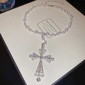 Macro shot of silver hollow cross necklace with crystals and white pearls on a box