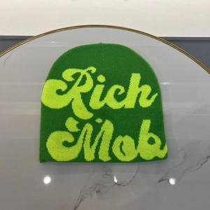 Detailed knit texture of green beanie with yellow Rich Mob lettering on marble surface
