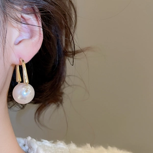 Detail of round pearl drop earrings in gold on model showing elegant fit and luster