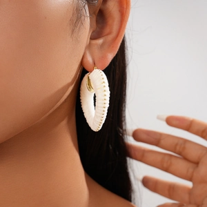 Detail of white woven heart earrings with gold bead accents on female model