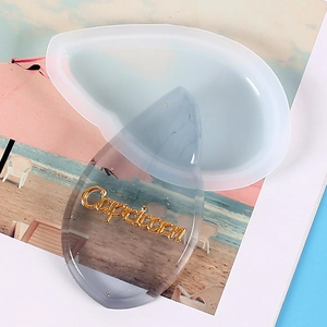 Silicone mold with resin drop pendant featuring Capricorn lettering on a beach photo background