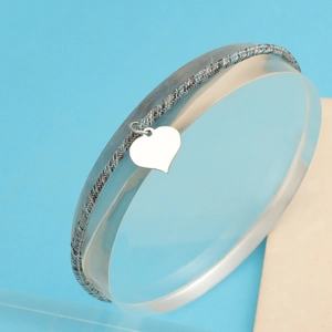Macro detail of silver mesh bracelet featuring a polished heart pendant on a display stand