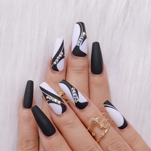 Close-up of long coffin press-on nails with black-white swirls and rainbow rhinestones