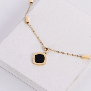 Gold necklace with square roman numeral pendant on a white textured stone pedestal