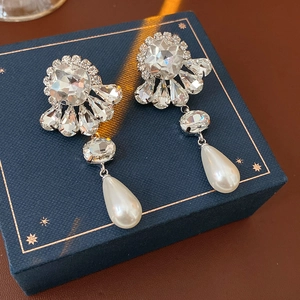 Macro detail of silver drop earrings with floral rhinestones and white teardrop pearls