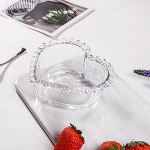 Heart-shaped glass dessert plate with beaded rim on a marble tray with fresh strawberries