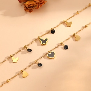 Détail d'un bracelet en acier doré avec pendentifs papillon noirs et breloques cœur