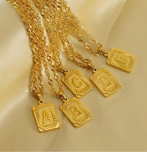 Detail view of 18K gold plated stainless steel square initial pendants on silk background
