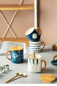 Close-up of Japanese style ceramic mugs with wooden lids, gold spoons and glaze patterns
