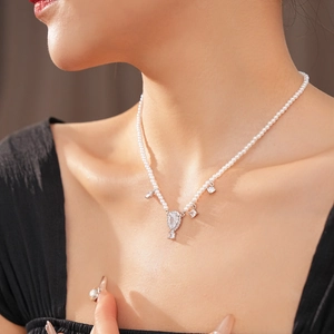 Macro shot of a pearl necklace featuring a diamond-set teardrop pendant on the neck