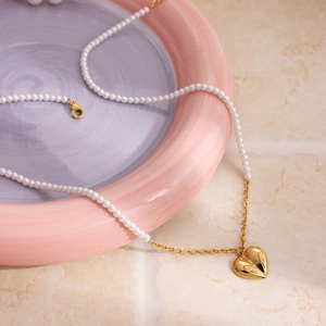 Close-up of pearl necklace featuring a textured gold heart pendant and lobster clasp detail