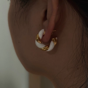 Detailed view of twist hoop earrings with gold metal and white enamel inlay on a model