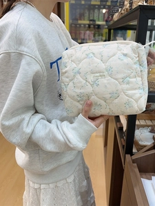 Quilted floral makeup bag with Sozukka label held by a model in a cozy indoor setting
