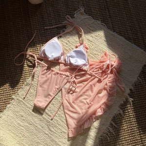 Detailed flat lay of pink three-piece bikini set with a sheer mesh ruffle sarong skirt