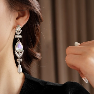 Detail of silver needle drop earrings with crystals and a white pearl on a model