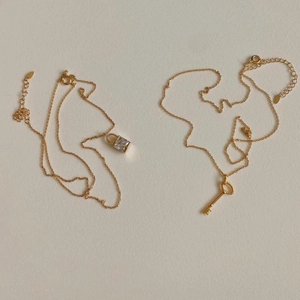 Detail of minimalist gold plated necklaces featuring square diamond lock and key pendants